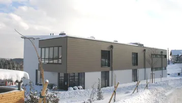 Modernes Gebäude mit Flachdach und großen Fenstern, umgeben von Schnee in einer ländlichen Umgebung.