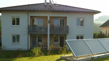 Mehrfamilienhaus mit zwei Balkonen, einem gepflegten Garten und einer Solaranlage auf dem Rasen.