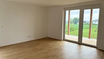 Heller Wohnraum mit Parkettboden und großzügigem Zugang zu einer Holzterrasse mit Grünblick.