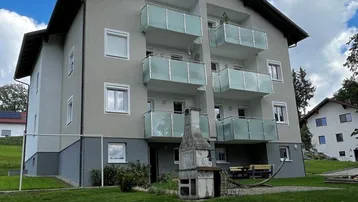 Mehrfamilienhaus mit modernen Glasbalkonen, umgeben von Grünflächen und einem Außenkamin.
