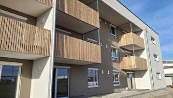 Modernes Mehrfamilienhaus mit Holzlamellenbalkonen und hellgrauer Fassade unter blauem Himmel.