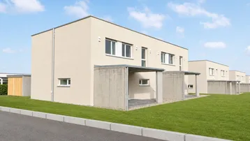 Moderne Reihenhäuser mit beigefarbener Fassade und gepflegtem Rasen in einer ruhigen Wohngegend.