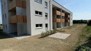 Modernes Mehrfamilienhaus mit Balkonen und noch unfertiger Außenanlage unter blauem Himmel.