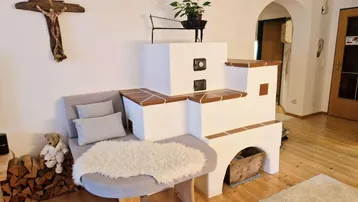 Detailansicht eines traditionellen Kachelofens mit integrierter Sitzbank und Holzlager.