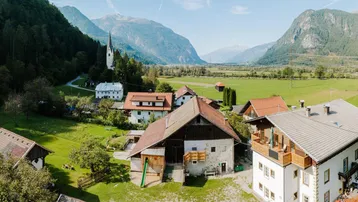 Panoramablick auf ein charmantes Dorf in einem grünen Tal, umgeben von majestätischen Bergen.