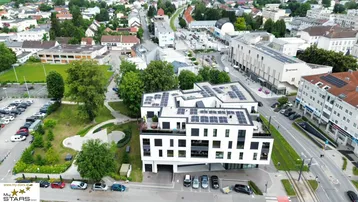 Luftaufnahme eines modernen Gebäudes mit Solarpaneelen auf dem Dach und umliegender Stadtlandschaft.