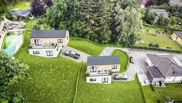 Luftaufnahme von zwei modernen Häusern mit großen Gärten und Zufahrten in grüner Umgebung.