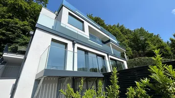 Moderne Architektur mit Glasbalkonen und viel Grün in sonniger Hanglage.