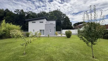 Modernes Einfamilienhaus mit großem Garten und gepflegter Rasenfläche unter bewölktem Himmel.
