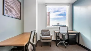 Modernes Büro mit zwei Arbeitsplätzen, einem Sessel und Blick auf die Stadt durch das Fenster.