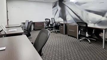Großraumbüro mit mehreren Schreibtischen, ergonomischen Stühlen und gemustertem Teppichboden.