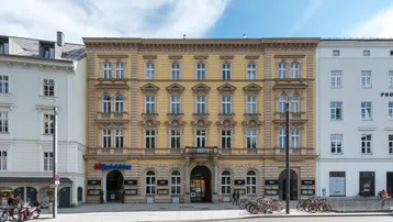Historisches Gebäude mit gelber Fassade und vielen Fenstern an einer belebten Straße.