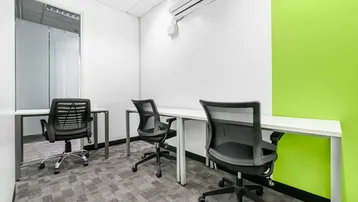 Kleines Büro mit drei Arbeitsplätzen, grüner Akzentwand und Teppichboden, ideal für konzentriertes Arbeiten.