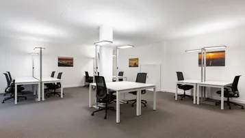 Heller, moderner Großraumbüro-Arbeitsbereich mit mehreren Schreibtischen und ergonomischen Stühlen.