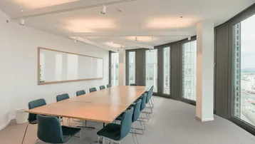 Moderner Konferenzraum mit großem Holztisch, bequemen Stühlen und weitreichendem Stadtblick durch die Fenster.