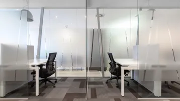 Modernes Büro mit Glaswänden, Teppichboden und ergonomischen Bürostühlen in einer offenen Arbeitsumgebung.