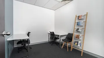 Kleines, helles Büro mit zwei Arbeitsplätzen, Teppichboden und einer Zeitschriftenablage.