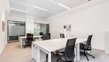 Modernes Großraumbüro mit mehreren Schreibtischen, ergonomischen Stühlen und Teppichboden.