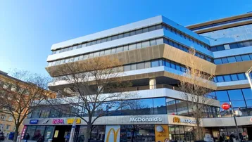 Modernes Geschäftsgebäude mit mehreren Etagen und großen Glasflächen an einer belebten Straße.
