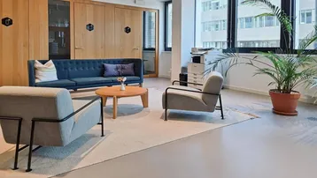 Moderner Büroloungebereich mit bequemen Sitzgelegenheiten, Holzwänden und großen Fenstern mit Stadtblick.