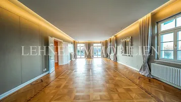 Großzügiges Wohnzimmer mit Fischgrätparkett, hohen Decken und bodentiefen Fenstern.