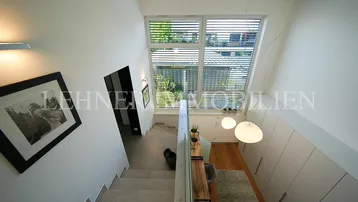 Moderner Treppenaufgang mit großem Fenster, das viel Tageslicht hereinlässt, und integriertem Stauraum.