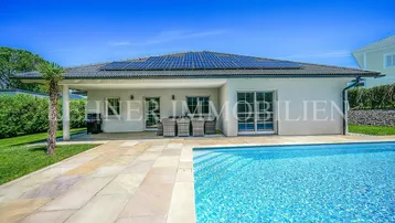 Modernes Einfamilienhaus mit Pool und Sonnenterrasse, umgeben von einem gepflegten Garten.