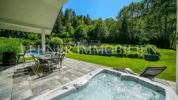Große gepflasterte Terrasse mit Whirlpool, Essbereich und Blick ins Grüne.