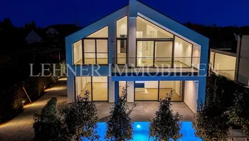 Moderne Villa bei Nacht mit beleuchtetem Pool und architektonisch ansprechender Fassade.