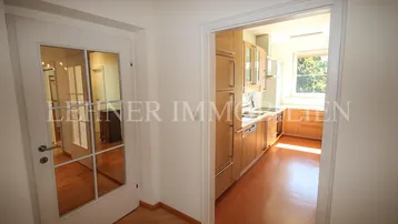 Heller Flur mit Holzboden und Blick in die angrenzende Küche mit Holzfronten.