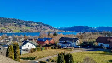 Panoramablick auf den See und die umliegende Berglandschaft mit Wohnhäusern im Vordergrund.