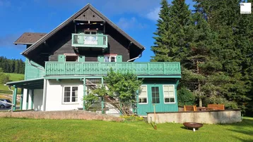 Traditionelles Landhaus mit grünen Balkonen, dunkler Holzfassade und einem Feuerplatz im Garten.