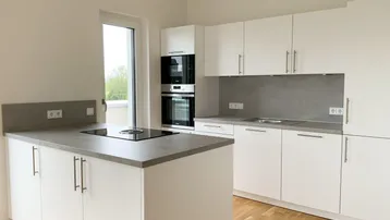 Moderne Einbauküche mit weißen Hochglanzfronten, grauen Arbeitsplatten und Induktionskochfeld auf der Kücheninsel.