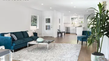 Helles, offenes Wohnzimmer mit bequemer Couch, Holzboden und Blick in die moderne Küche.