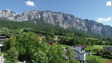 Panoramablick auf eine beeindruckende Berglandschaft mit grünen Hügeln und vereinzelten Häusern.