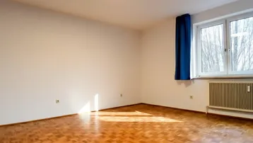 Heller, leerer Wohnraum mit Parkettboden und großem Fenster, das viel Sonnenlicht hereinlässt.