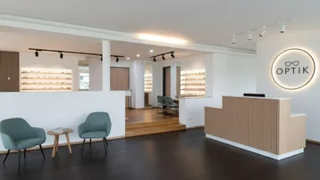 Moderner Empfangsbereich eines Optikergeschäfts mit dunklem Holzboden und stilvoller Beleuchtung.