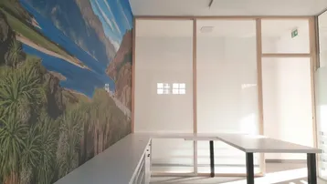 Modernes Büro mit Glaswänden, Schreibtischen und einer Wandtapete mit Berglandschaft.
