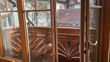 Heller Innenraum mit Holzboden und Zugang zu einem Balkon mit traditionellem Holzgeländer.