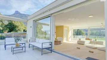 Helles Wohnzimmer mit großen Schiebetüren, die zu einer möblierten Terrasse mit Bergblick führen.