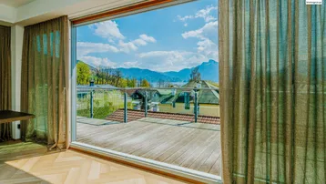 Helles Zimmer mit Fischgrätparkett und großen Schiebetüren, die auf eine Terrasse mit See- und Bergblick führen.
