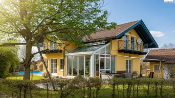 Großzügiges Einfamilienhaus mit gelber Fassade, Wintergarten, Balkonen und einem weitläufigen Garten mit Pool.