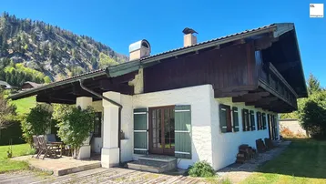 Traditionelles Haus im alpinen Stil mit Holzbalkonen und Bergblick unter blauem Himmel.
