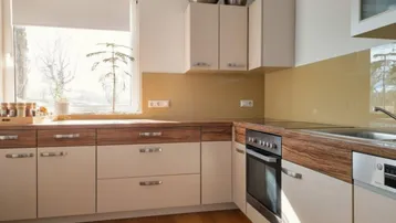 Moderne Küche mit hellen Schränken, Holzarbeitsplatten und integrierten Geräten, gut beleuchtet durch ein Fenster.