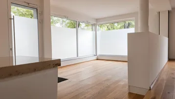 Heller Wohnbereich mit Holzboden, großen Fenstern und einer Theke im Vordergrund.