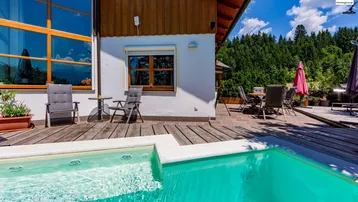 Geräumige Holzterrasse mit kleinem Pool und Sitzgelegenheiten vor dem Haus mit Waldblick.