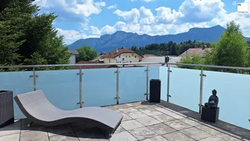 Geräumige Terrasse mit Liegestuhl und Glasgeländer, bietet einen weiten Blick auf die Berge.