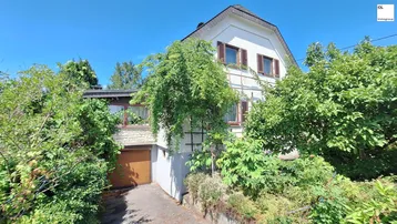 Traditionelles Einfamilienhaus mit Satteldach, Garage und üppiger Begrünung in sonniger Lage.
