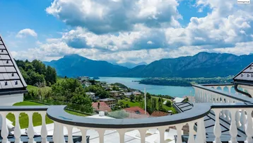 Panoramablick von einem eleganten Balkon auf einen malerischen See und die umliegende Berglandschaft.