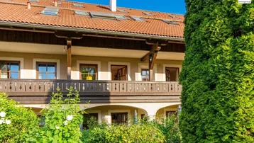 Traditionelle Fassade mit Holzbalkonen, Dachfenstern und üppiger grüner Bepflanzung im Vordergrund.
